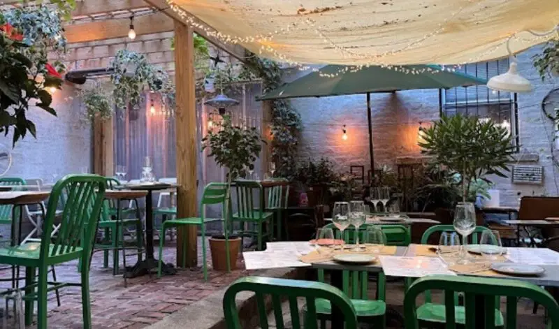 A charming outdoor dining area at Terre restaurant with green chairs, plants, and soft lighting under a canopy