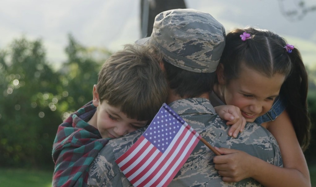 Soldier hugs his kids in front of the house