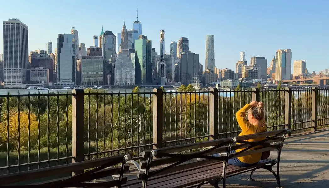 A woman sits on a park bench, enjoying the panoramic view of the New York City skyline