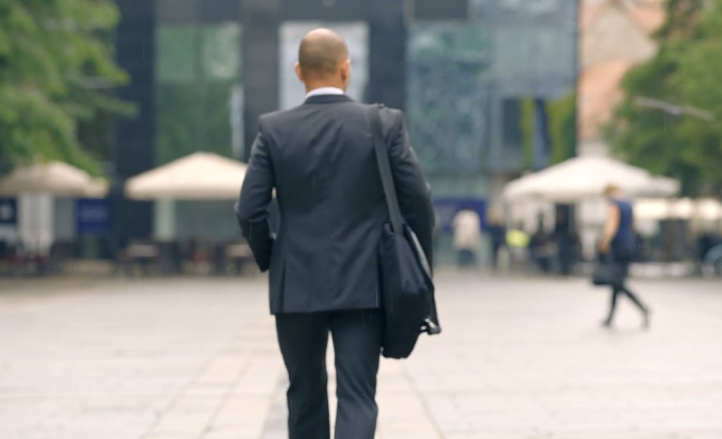 A man in a dark suit walks purposefully through a bustling city square