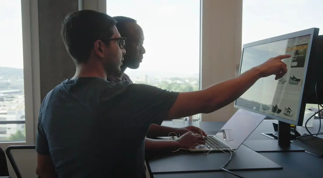 Two colleagues collaborate, reviewing product details on a large screen