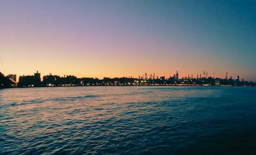 A tranquil evening view of the New York City skyline, bathed in the soft hues of a fading sunset