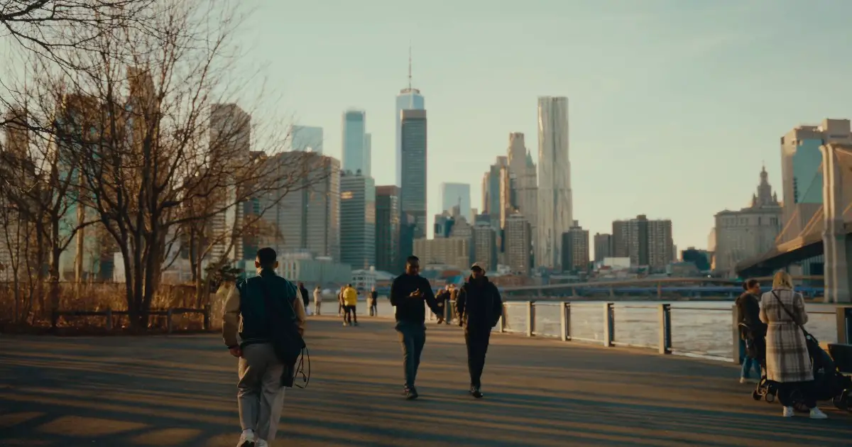 A tranquil scene of people walking along a riverside path in Brooklyn, NYC