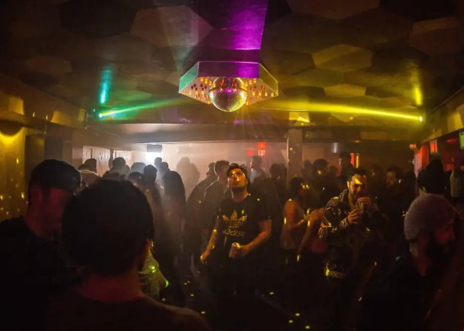 A lively dance floor with a golden disco ball, flashing lights, and clubgoers enjoying the music