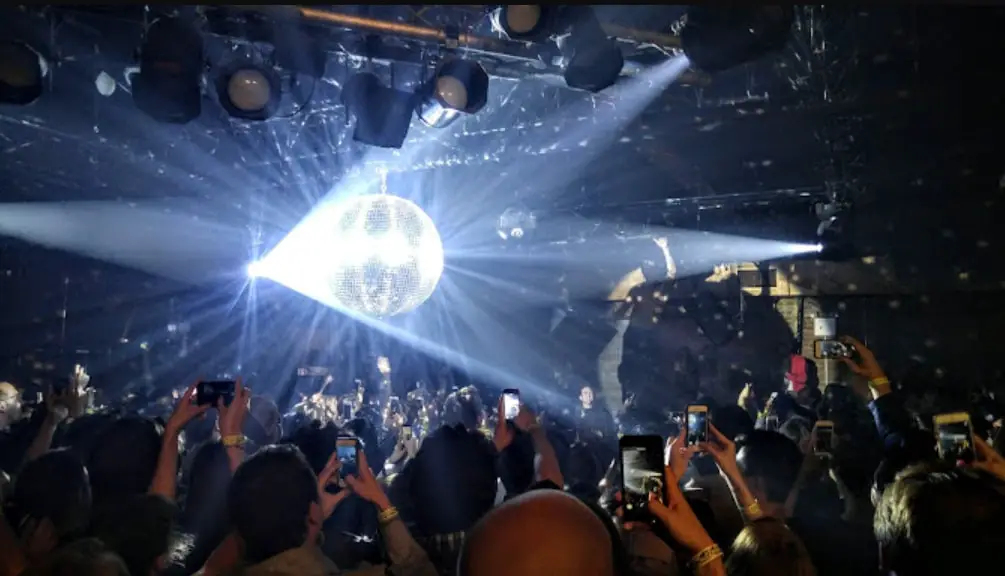 A nightclub with a massive disco ball reflecting bright lights over a crowd taking photos