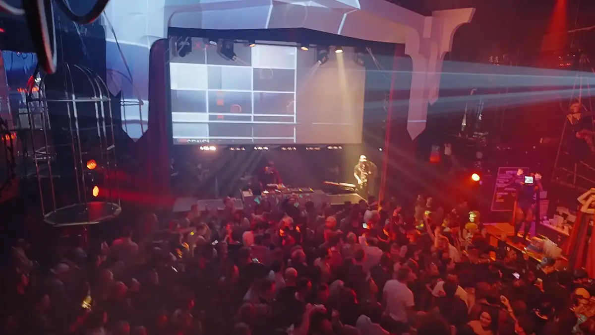 A nightclub with a DJ performing in a futuristic setting with an energetic crowd