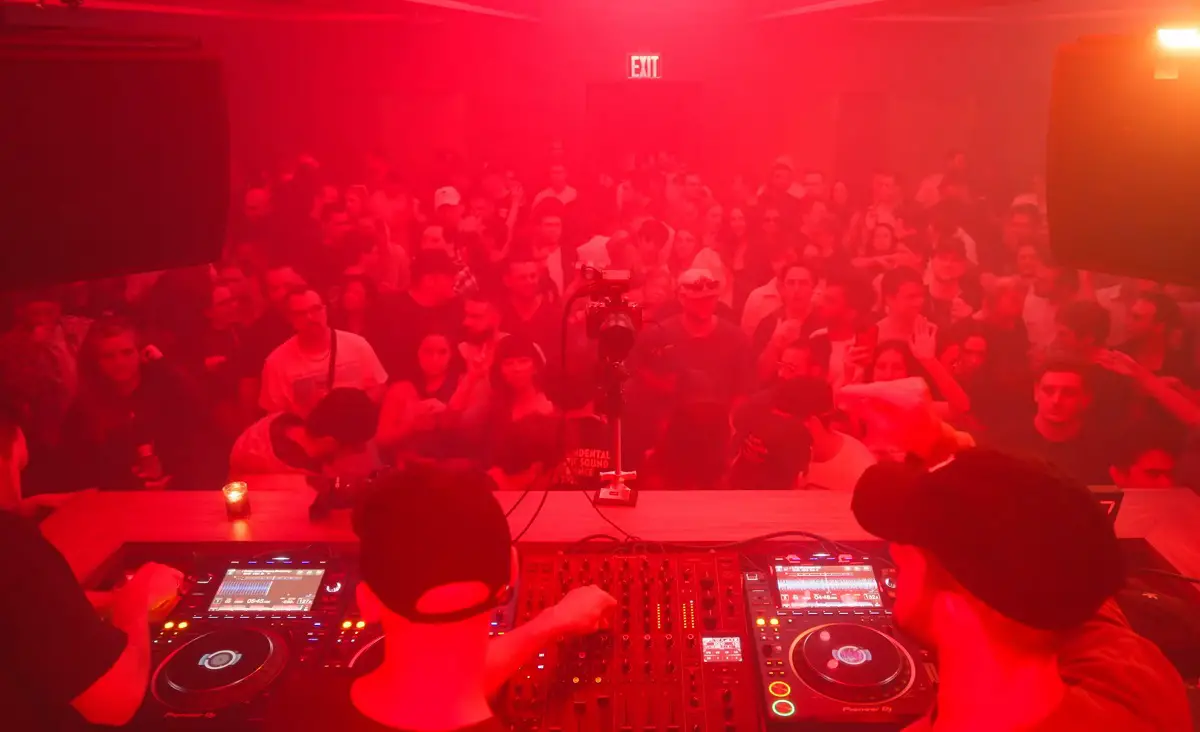 A DJ performing in a red-lit club with a packed crowd enjoying the music