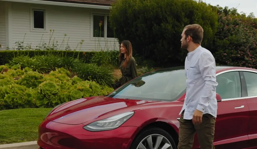 A couple approaches a red electric car