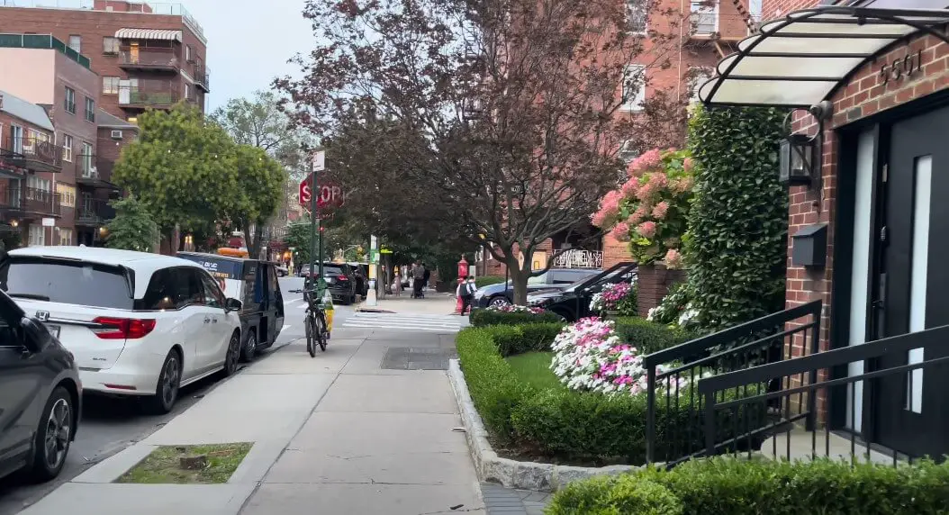 A quiet residential street scene, featuring parked cars and pedestrians crossing