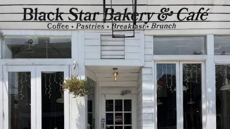 White-painted exterior of a bakery and cafe with bold signage and hanging plants near the entrance