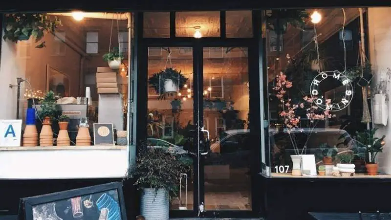 Charming storefront with plants and warm lighting, inviting passersby into a cozy neighborhood cafe