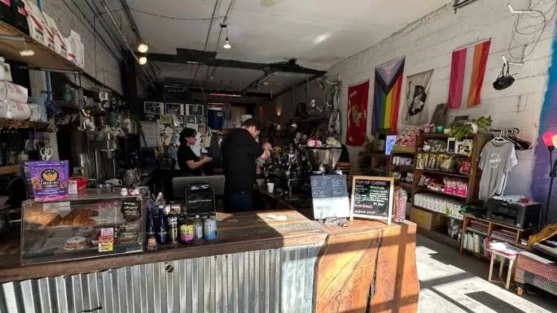 Industrial-style coffee bar with eclectic decor, snacks on display, and baristas preparing drinks — a unique spot among coffee shops